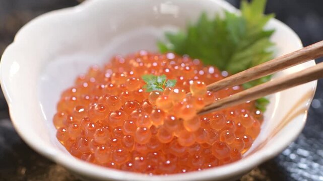 Fresh salmon roe ikura cured in soy sauce presented on elegant white ceramic plate with shiso leaf
