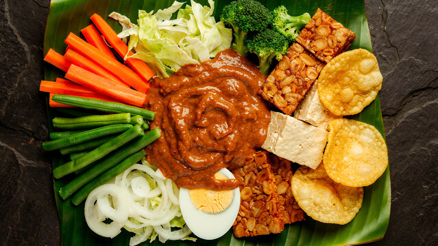 A flat-lay shot featuring colorful Indonesian gado-gado salad&mdash;complete with peanut sauce, assorted vegetables, tofu, tempeh, and crackers served on a banana leaf&mdash;a traditional Indonesian dish.