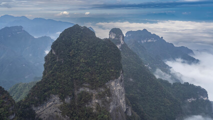 Obraz premium Picturesque mountain landscape. High cliffs. Green vegetation on steep slopes and peaks. Blue sky, clouds. China. Zhangjiajie. Tianmen Mountain