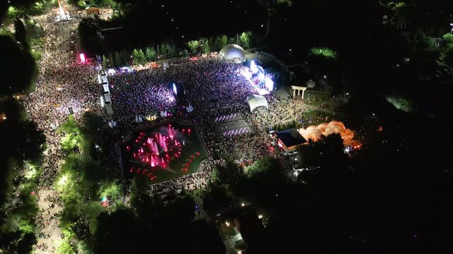 4K Aerial Drone View of Massive Outdoor Night Music Festival with Dancing Crowd,Concert Stage and Colorful Light Show in City.People dancing in front of a brightly illuminated concert stage with light