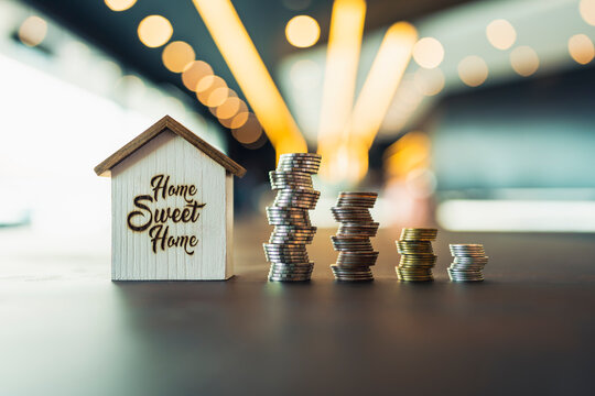 Real estate house model with growing stacks of money coins. Concept of property mortgage, home loan, refinance, interest rate, down payment, and insurance.
