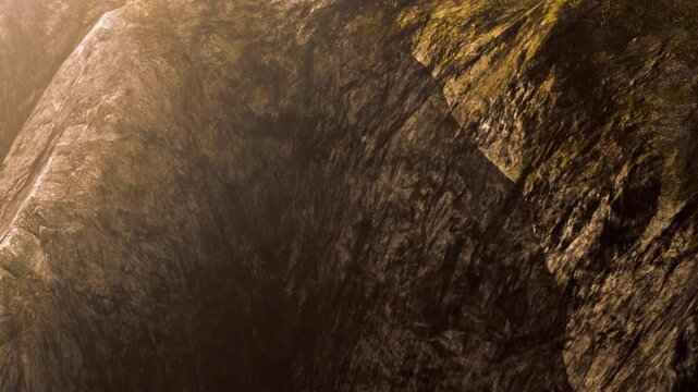 Sunlight shines on a large rock formation with rough textures and shadows. The setting showcases natural elements in a remote area during daytime.
