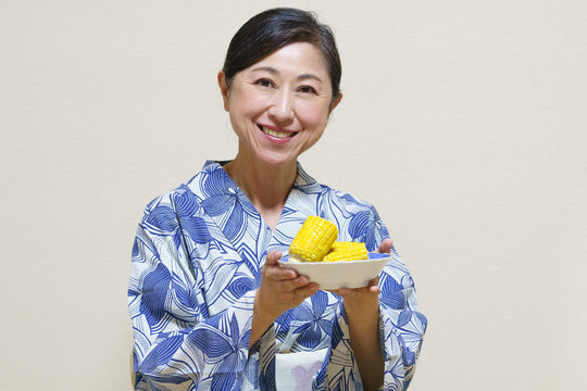 浴衣を着て茹でトウモロコシを差し出す女性