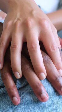 A close-up of a diverse couple's hands gently interlocking fingers, symbolizing love, intimacy, and profound connection. This tender embrace on denim jeans highlights unity and affection in a heartwar