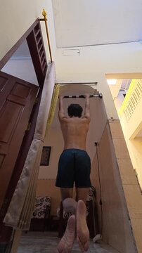 Vertical shot of shirtless man performing scapula pull up exercise from behind view, mobile fitness content