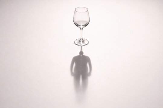 Transparent wine glass casting a shadow resembling a human figure on a textured surface, showcasing interplay of light and shadow in a minimalist composition