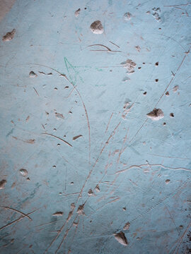A vertical close-up shot focusing on a rough concrete wall covered in light blue paint, showing numerous scratches, dents, and imperfections.