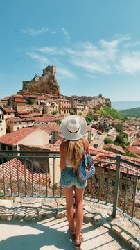 Back view of woman traveler with hat and backpack looking at Frias medieval village in Burgos Spain
