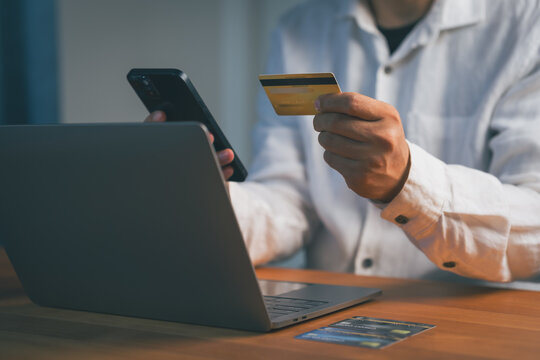 Man engages in online shopping and e-commerce, using a credit card for payment. He accesses mobile banking on a smartphone and internet via laptop for this finance transaction.