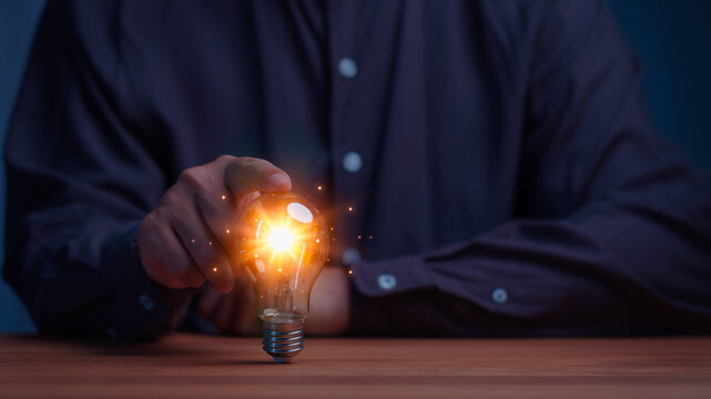 Businessman touching a glowing light bulb with sparks. This concept represents a bright business idea, innovation, technology, creativity, inspiration, and future success.