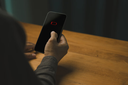 Person holding a smartphone with a red low battery warning icon on a black screen. Represents modern technology, power loss, and mobile connection anxiety in daily life.