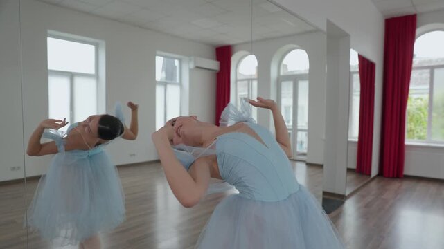 Beautiful young ballerina in a light blue tutu gracefully practicing classical dance moves, performing elegant pirouettes and arm movements in a professional studio with large mirrors