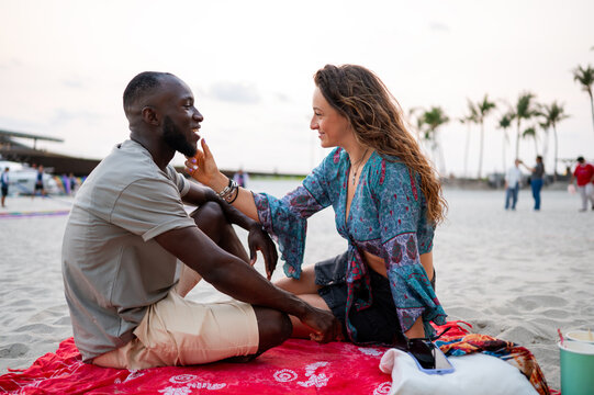 A romantic young couple enjoying a peaceful picnic on a sandy beach at sunset, intimate conversation