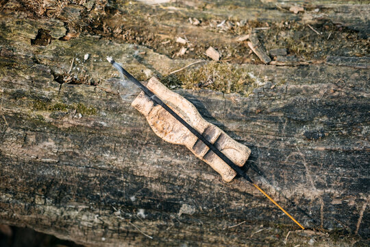 Burning incense stick on ceramic holder rests on weathered log outdoors. Incense smoke closeup, burning incense smoke trail, meditative smoke, Wellness brand product.