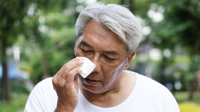 Tired and uncomfortable old asian senior man wiping his face with refreshing cold wet towel, trying to relieve from heavy sweating and outdoor summer heat wave