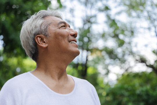 Relaxed happy refreshing old retired senior Asian man showing smiling expression in urban park, good summer, summer wellness, sunlight exposure concept image
