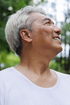Relaxed happy refreshing old retired senior Asian man showing smiling expression in urban park, good summer, summer wellness, sunlight exposure concept image