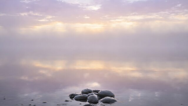 Serene water reflection with scattered stones and soft misty sunlight creating a peaceful, ethereal natural landscape