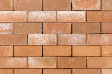 Solid wall constructed from textured rectangular light brown and terracotta bricks in a running bond pattern. © wannasak