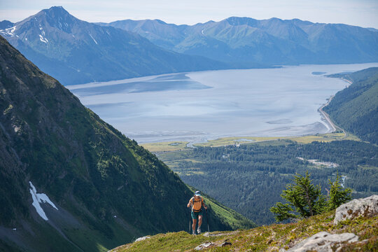 Woman hiking a steep alpine trail in Alaska with inlet in background