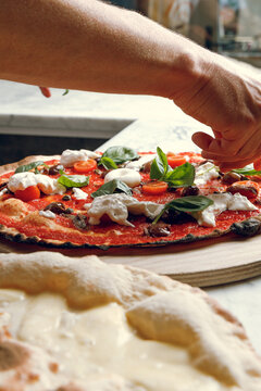 A pizzaiolo adds mozzarella cheese to a freshly baked pizza