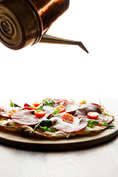 A pizzaiolo drizzles olive oil over a freshly baked pizza