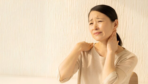 首を押さえて痛みに耐える日本人女性・寝違えや肩こりイメージ・コピースペースあり