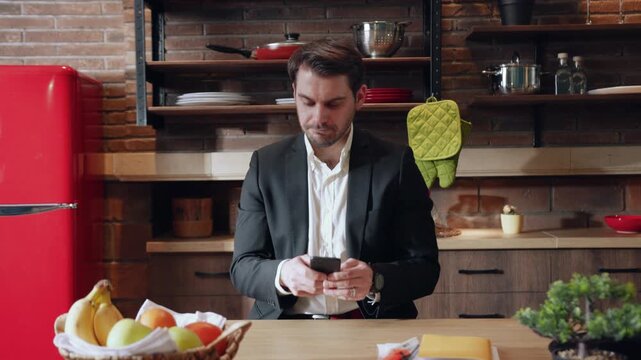A businessman uses his smartphone in a modern kitchen, managing tasks related to work