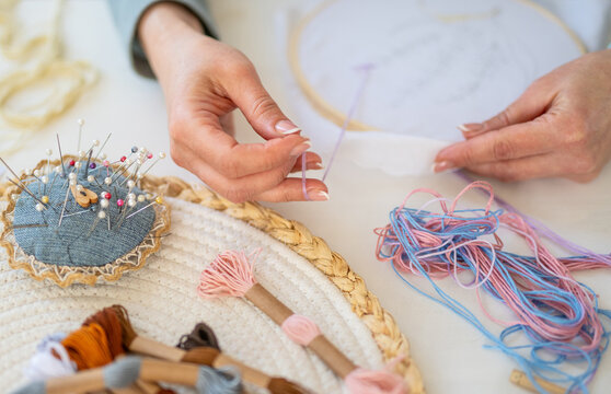 A woman creates an embroidery design using a pencil and colorful threads, surrounded by scissors and fabrics on a table