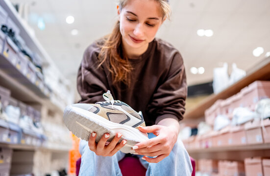 Happy Woman Examining Sneakers While Picking Sports Shoes In Shop