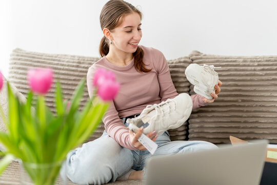 Happy Girl Sitting On Couch At Home Holding Sneakers After Buying Them From An Online Shoe Store