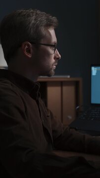 Side view of software engineer using AI digital assistant on his computer while programming at home office workspace with artificial intelligence interface on screen. Vibe coding, AI agents concept.