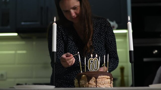 Young woman lighting candles on a birthday cake with number 60 candles. Close family celebration preparation before a milestone birthday gathering.