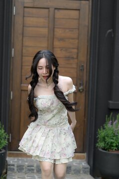 Young woman in light floral dress with long dark hair standing outdoors near wooden gate
