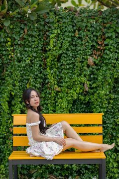 Woman Relaxing on Bright Yellow Bench with Green Leafy Background