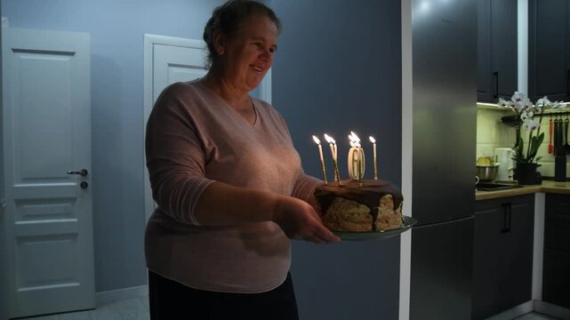 Mother carries a birthday cake with lit candles and number 60 toward the dining table, where the father, adult children and grandchildren are gathered.