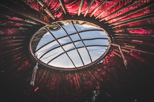 A window in the roof of a traditional Asian yurt, a round wooden structure, and interior elements in a yurt with red paneling