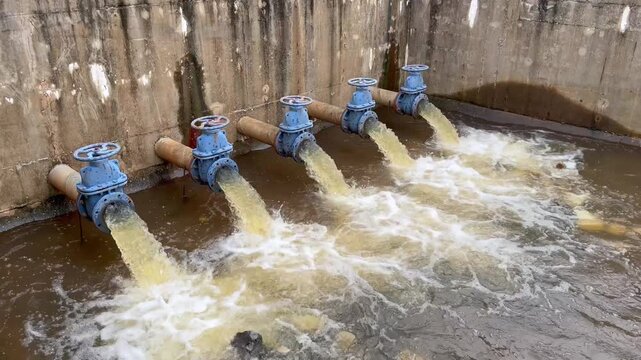 Academic engineering footage demonstrating industrial water drainage infrastructure. Video showcases large pipeline gate valves discharging liquid flow for flood management lesson