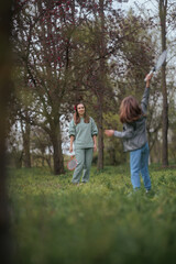 Fototapeta premium Mother And Daughter Playing Badminton Outdoors In Green Sunny Park. Happy family enjoys active leisure time together hits shuttlecock with racket outside 