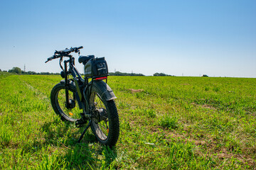 Fototapeta premium Rear view of an electric mountain bike with thick fat tires parked in a vast green meadow under a clear blue sky 