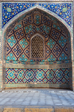 Ornate mosaic tilework niche on Nadir Divan Begi Madrasah in Bukhara, Uzbekistan. Geometric and floral patterns in turquoise and blue decorate the pointed arch facade. Ideal for travel publications.