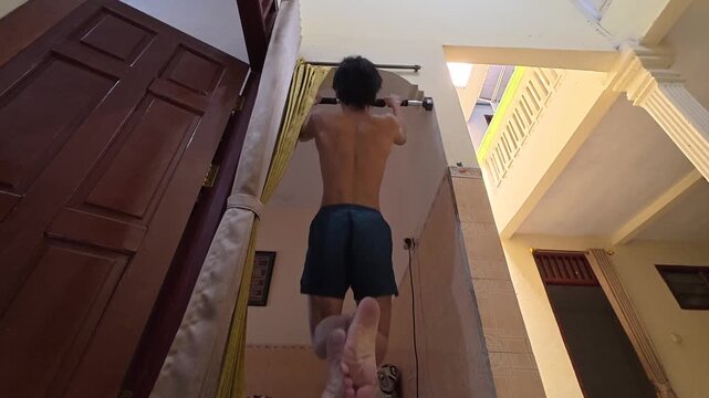 Back view of a shirtless man doing modified pull ups with feet on the floor at home, inverted row exercise