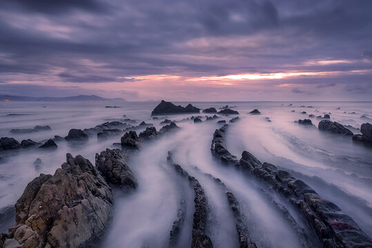 Long exposure seascape at Barrika Beach with dramatic rock formations, misty waves and colorful sunset clouds over the Cantabrian coast