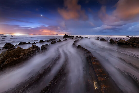 Long exposure seascape at Barrika Beach with dramatic rock formations, misty waves and colorful sunset clouds over the Cantabrian coast