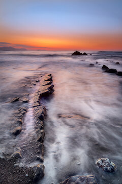 Long exposure seascape at Barrika Beach with dramatic rock formations, misty waves and colorful sunset clouds over the Cantabrian coast