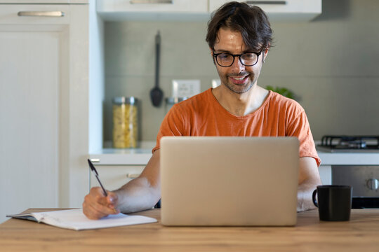 Cheerful freelancer guy working on a laptop at home, Sitting at the desk with laptop, making notes, Enjoying freelance Job.
