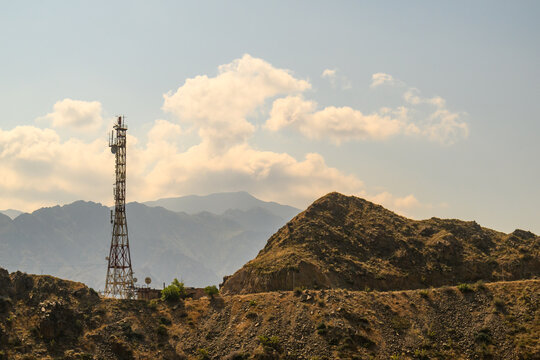 Cell tower rises above arid mountains with scattered clouds