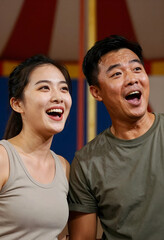 Fototapeta premium Excited asian couple with open mouths looking up, expressing surprise and joy at an event or performance