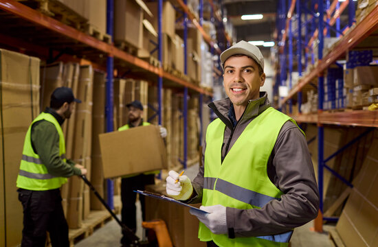 Worker in warehouse performs inventory on clipboard. Logistics loader manages delivery as colleagues move boxes on shelves, keeping shipping accurate. Concept of dependable warehouse logistics.