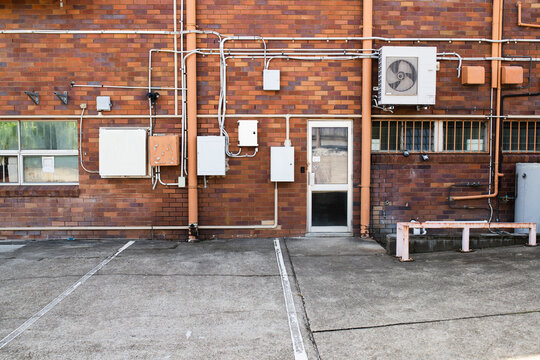 Rear exterior brick wall of commercial building with electrical panels, piping, and service door
